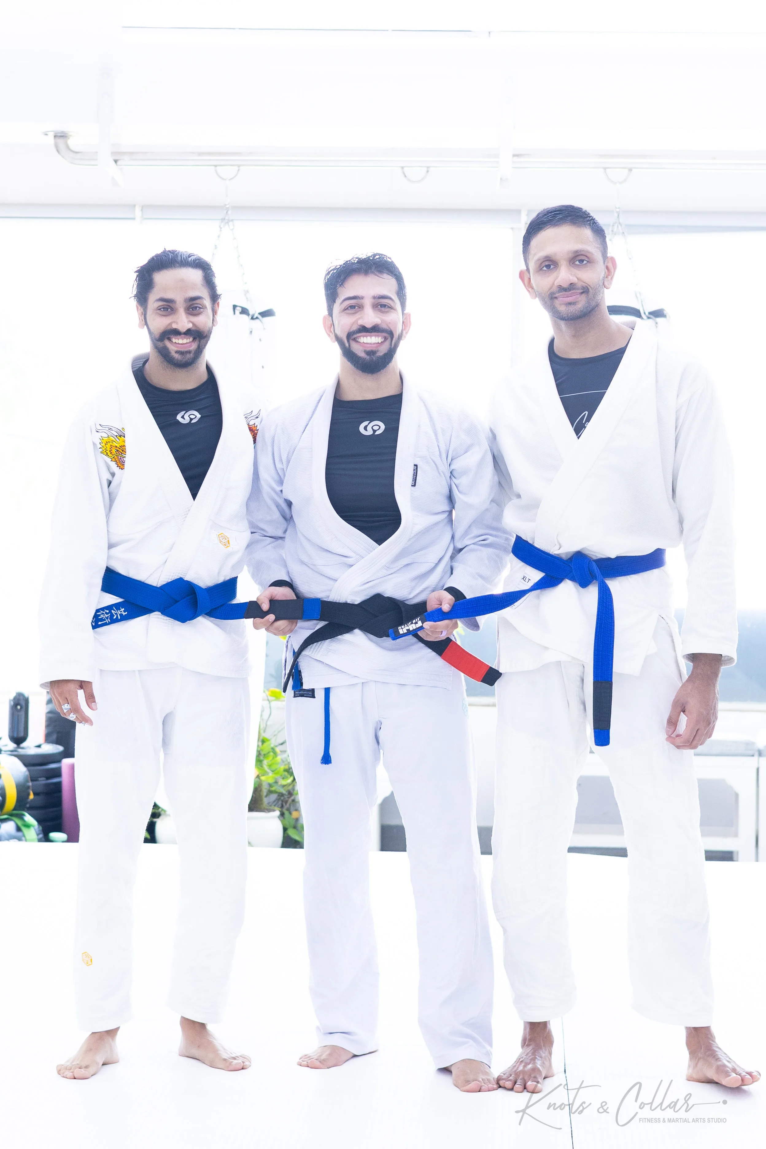 Multiple BJJ students receiving blue belt promotions in a ceremony at Knots & Collar