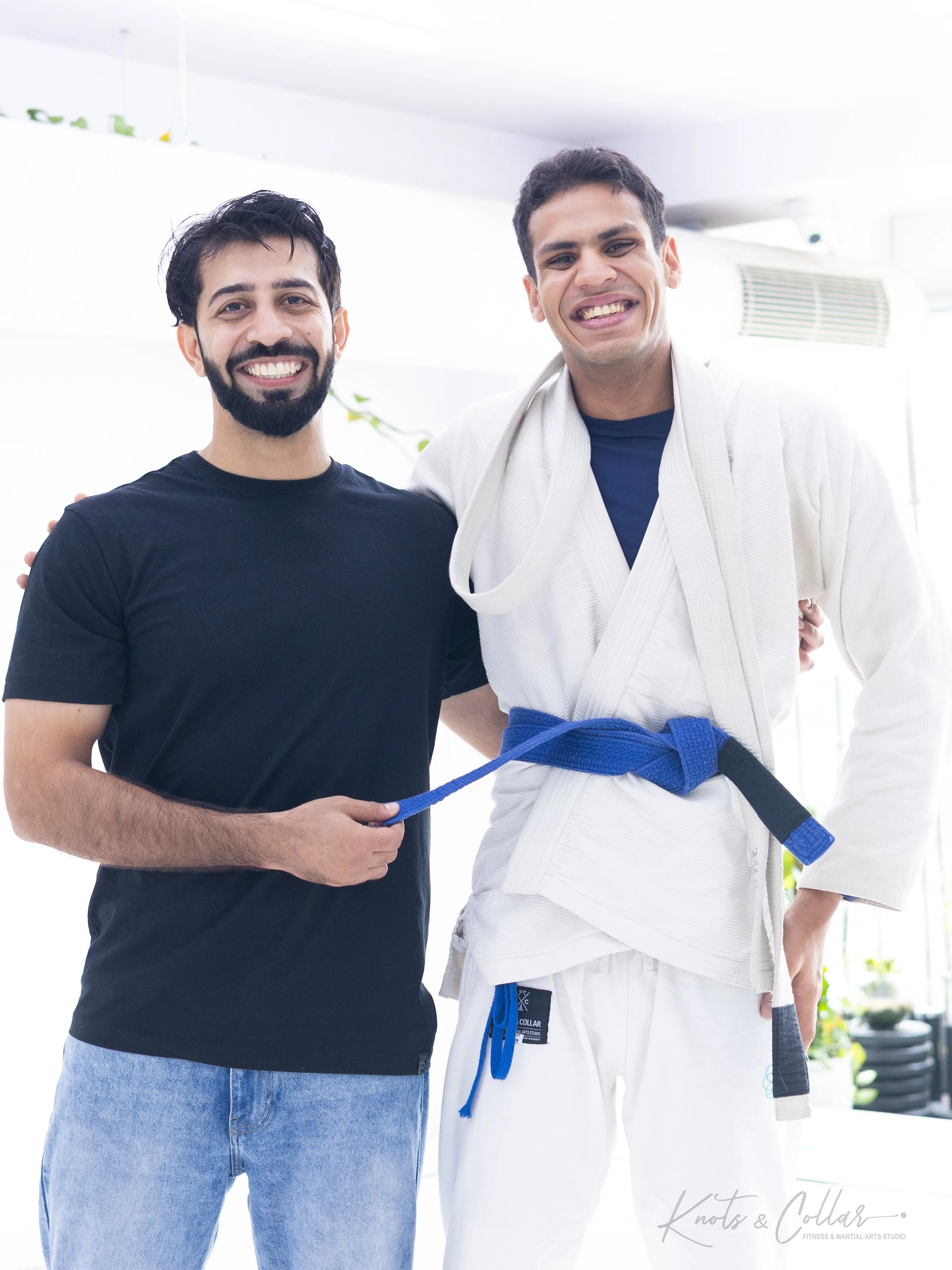 BJJ blue belt promotion ceremony — instructor tying the belt on a newly promoted student