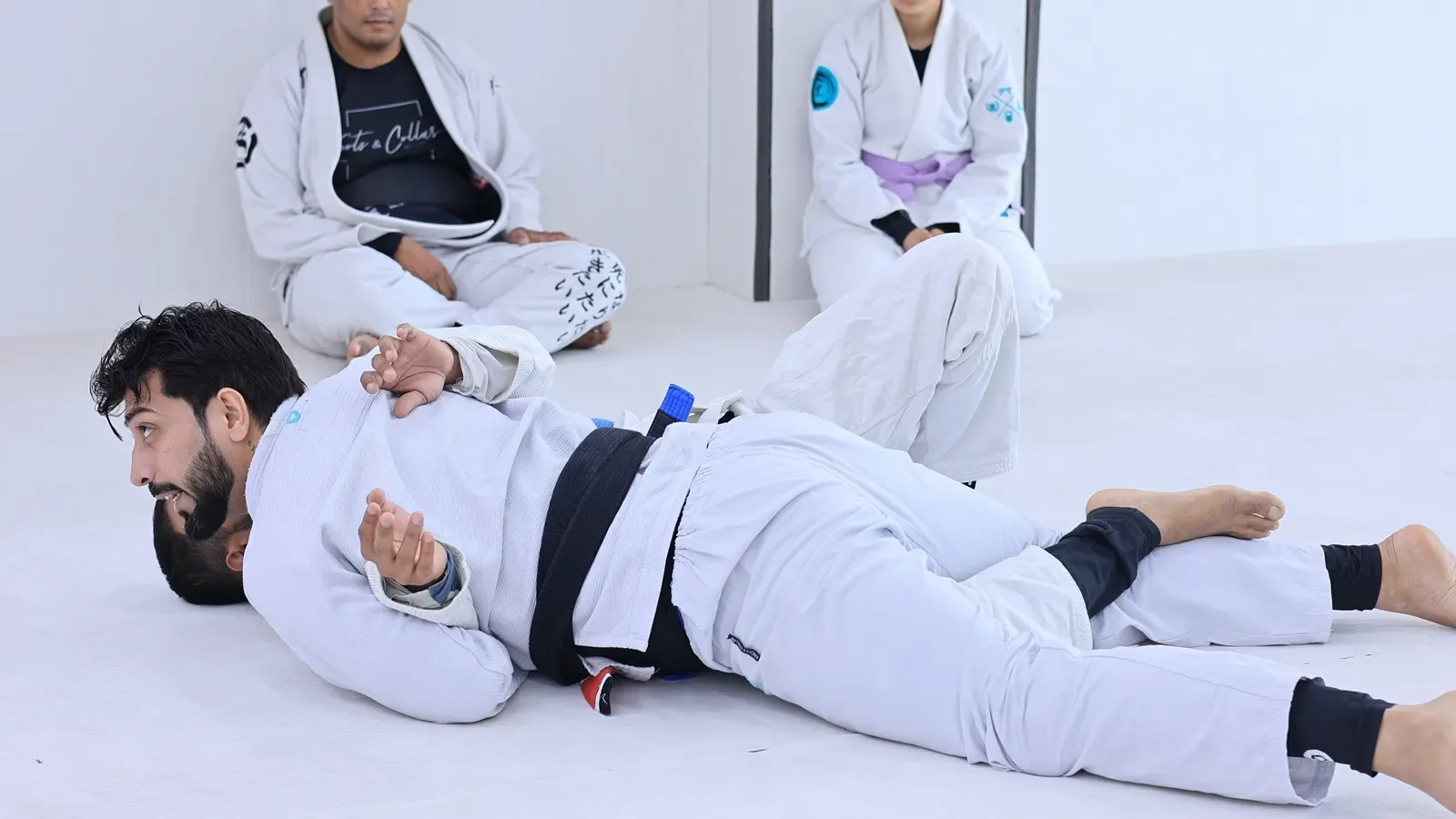Top player staying flat and heavy on the mat while passing half guard, as students watch