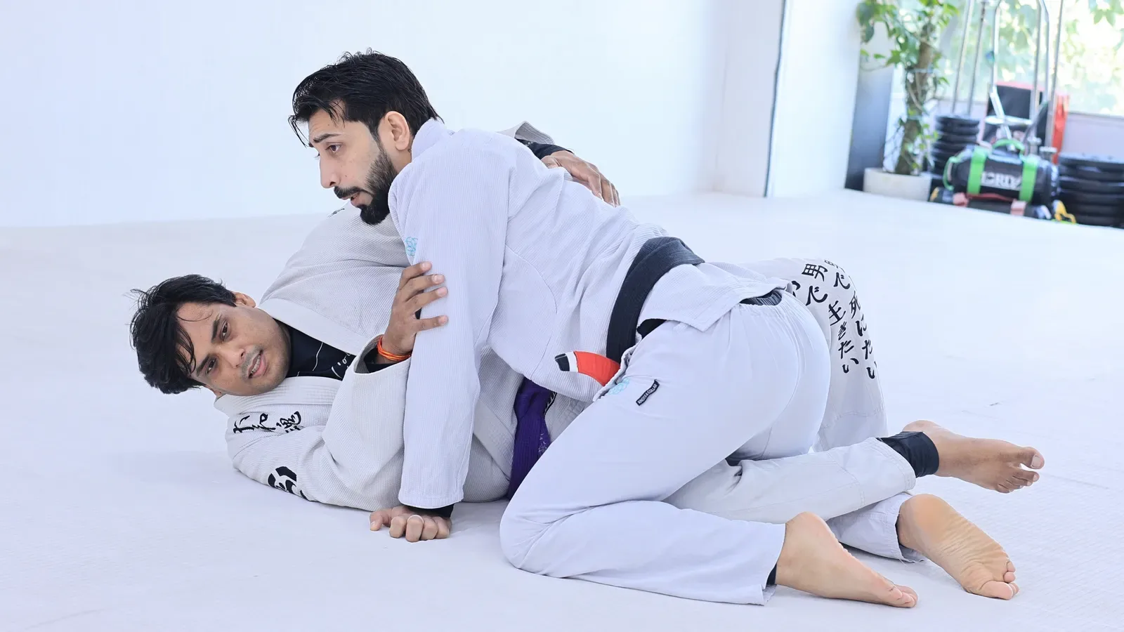 Black belt on top in half guard with a belt grip, starting a pressure pass at Knots & Collar, New Delhi