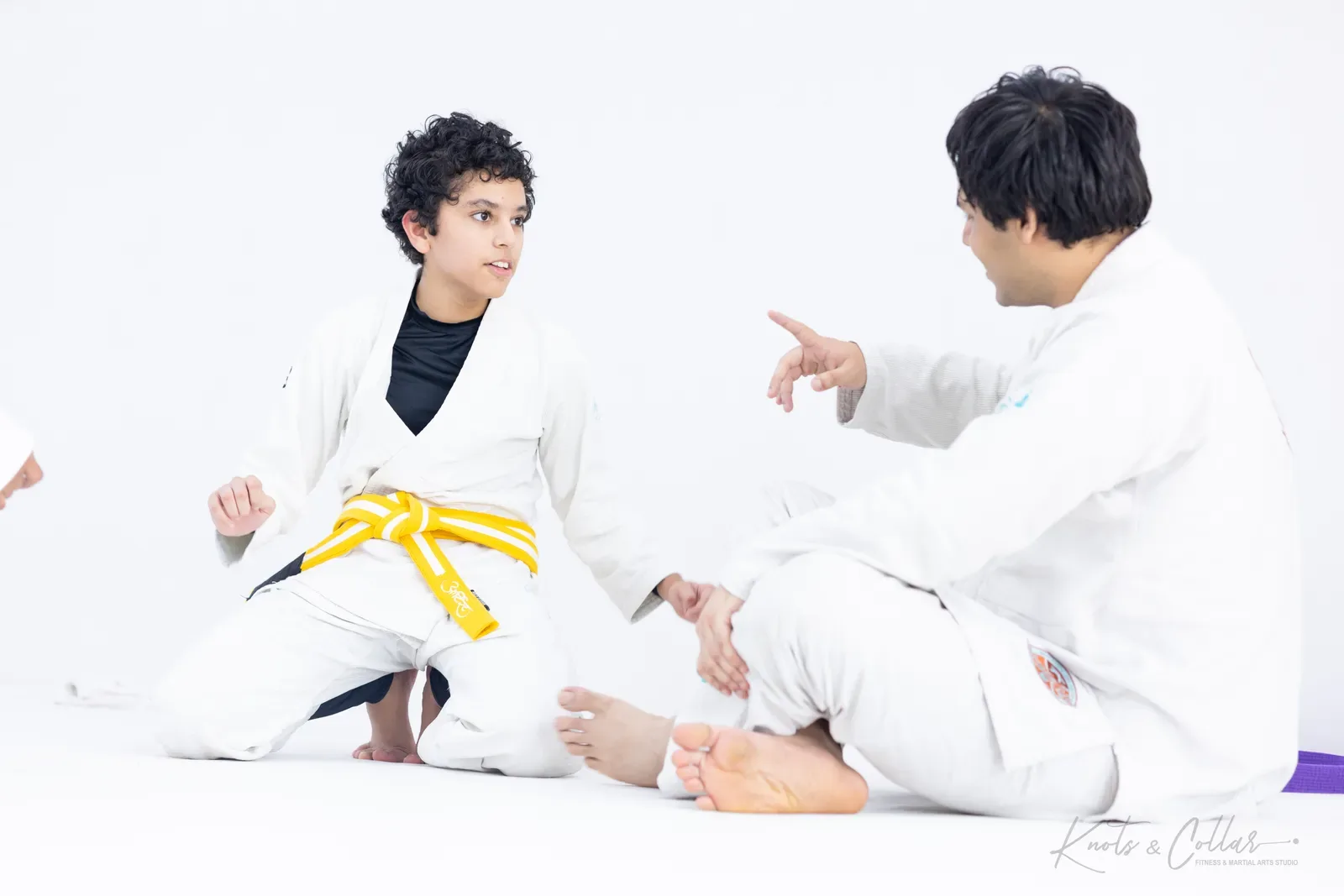 A coach talking a young yellow belt through a position at Knots & Collar kids BJJ in Delhi