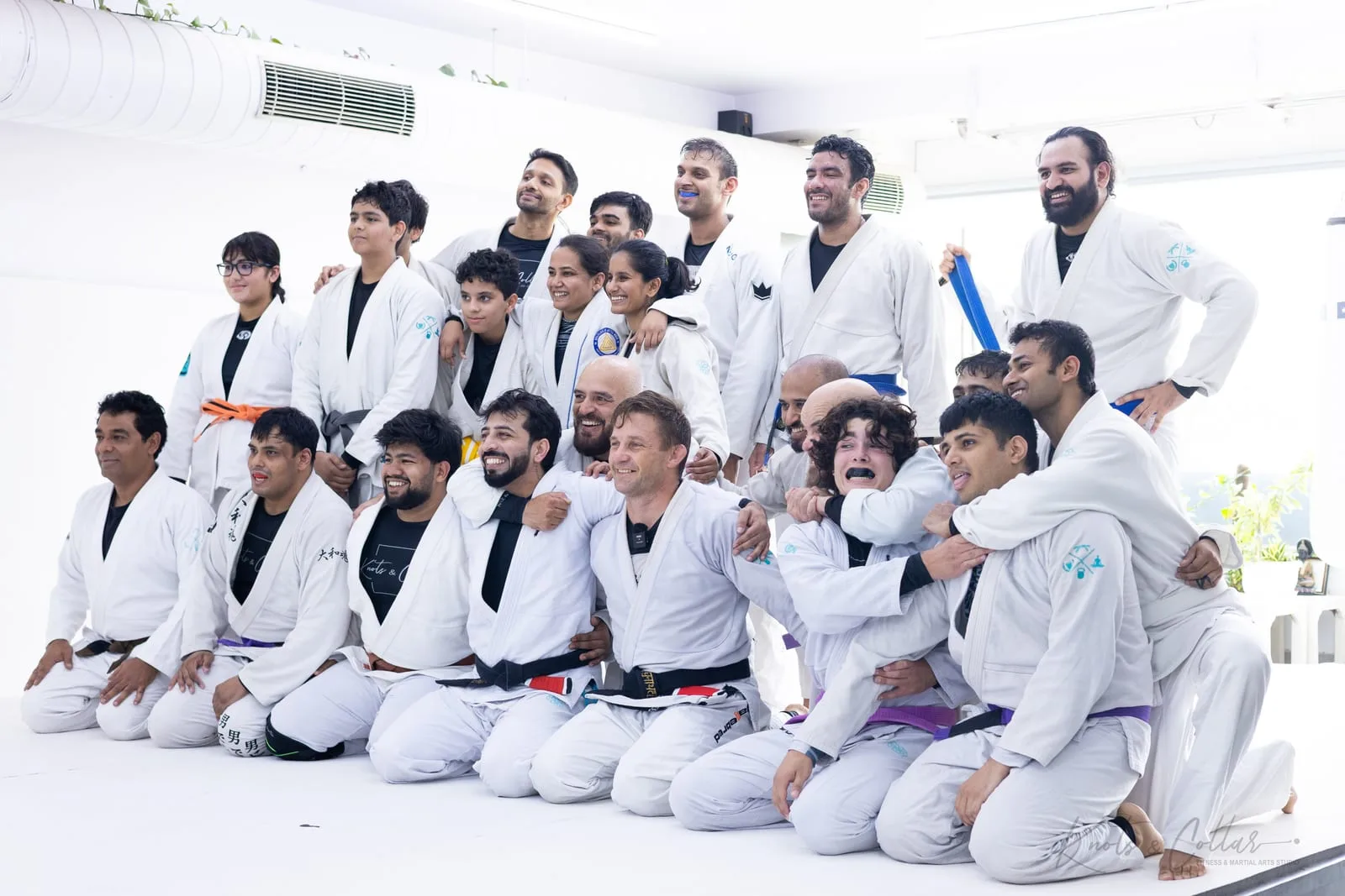 The Knots & Collar team kneeling and standing together on the white mats with visiting CSW black belt Professor Jad Strutzel after a Judo throws class for jiu-jitsu in South Delhi