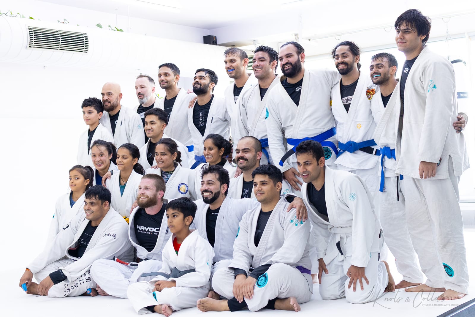 The Knots & Collar gi team photographed with visiting Professor Aaron White of Havoc MMA Denver on the white mats of the Defence Colony studio, New Delhi