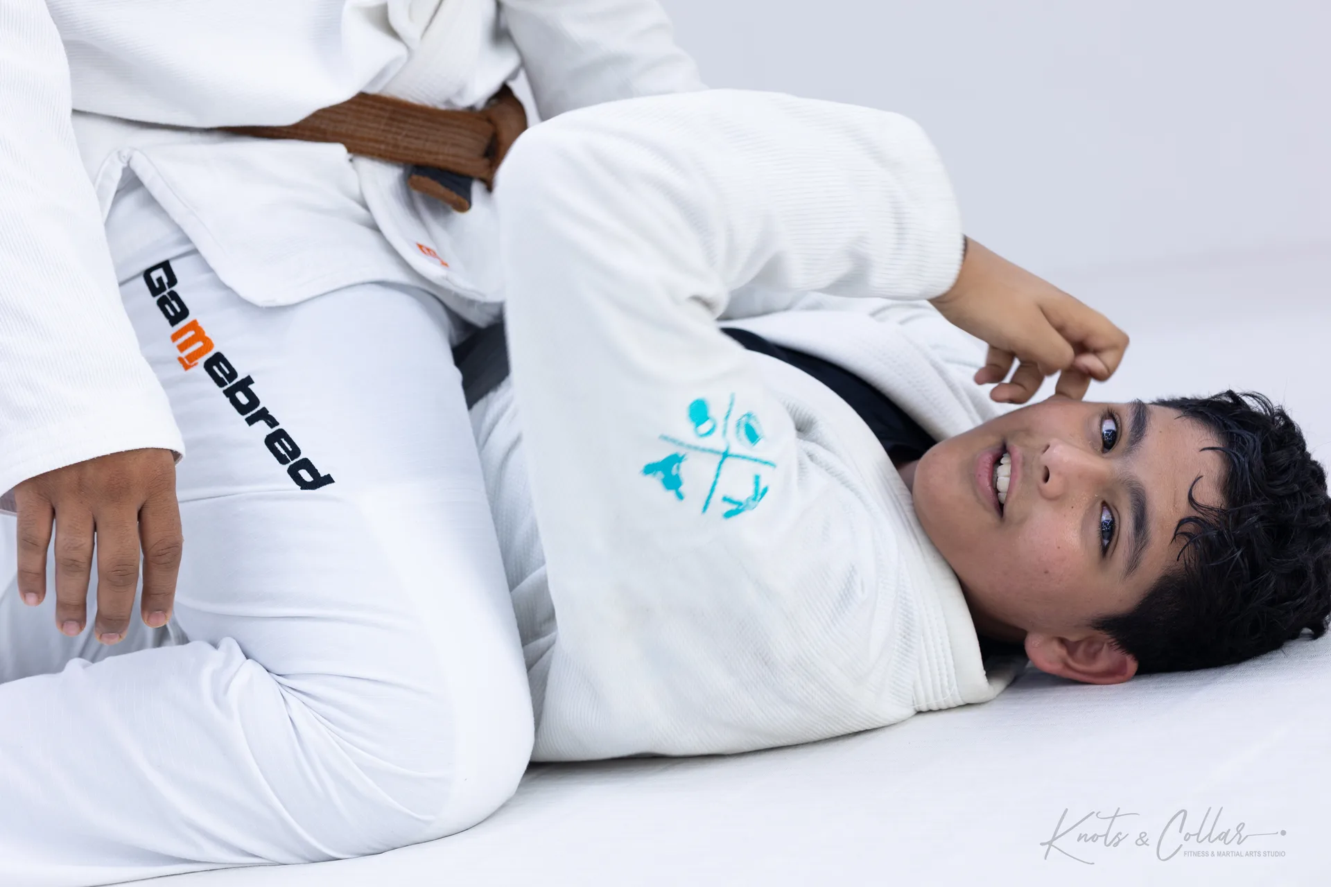 A teenage student in a white gi training Brazilian Jiu-Jitsu on the ground at Knots & Collar, Defence Colony, New Delhi