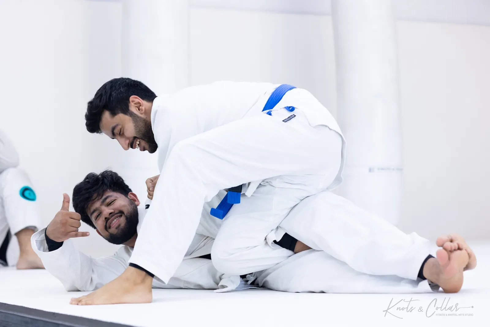 Two students in white gis smiling during a light Brazilian jiu-jitsu roll at Knots & Collar, Defence Colony, New Delhi